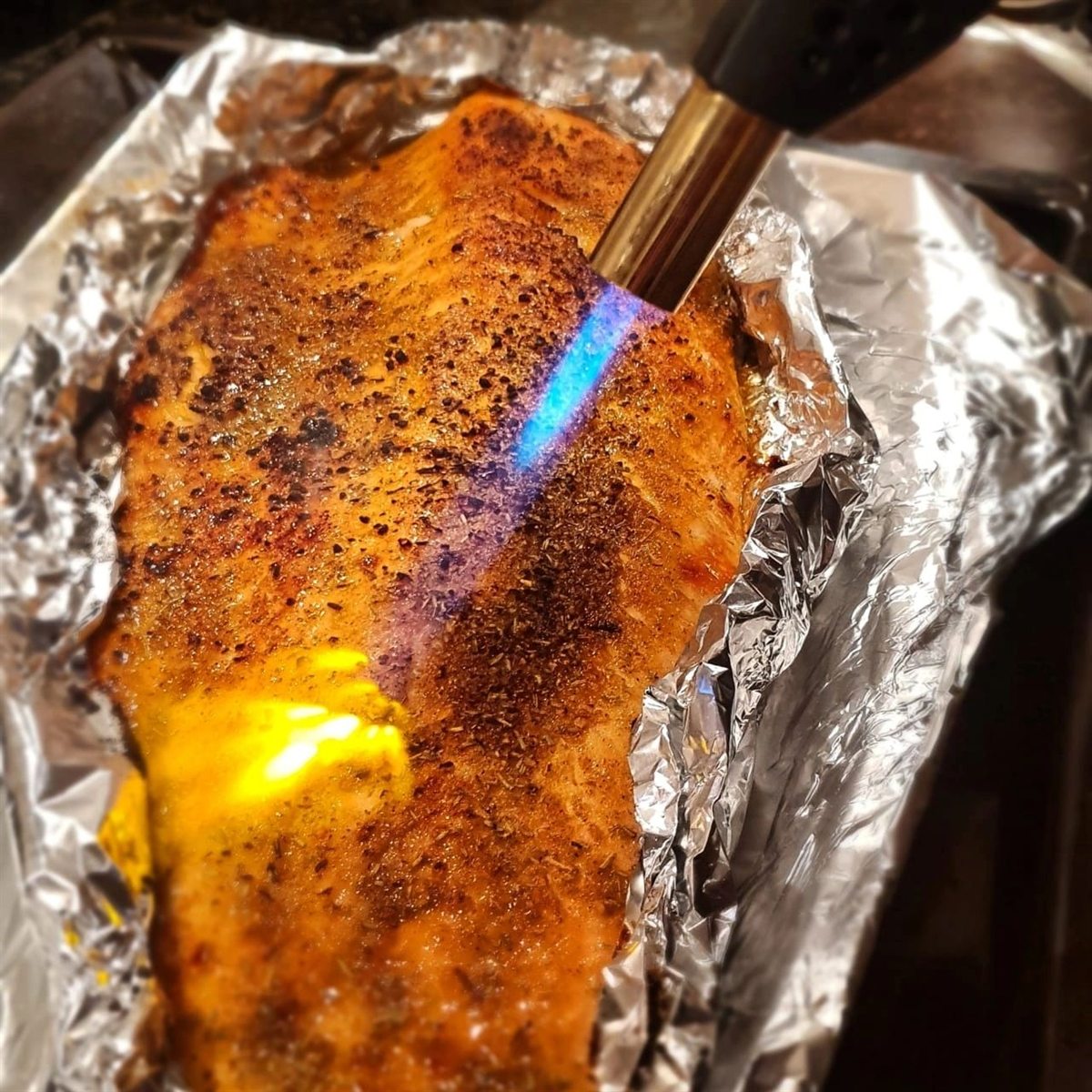 A whole fillet of cured salmon being finished with a kitchen blowtorch